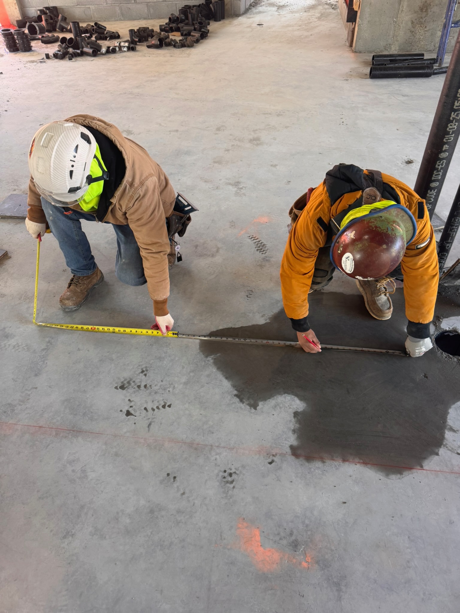 Two crew members measuring and marking a concrete floor